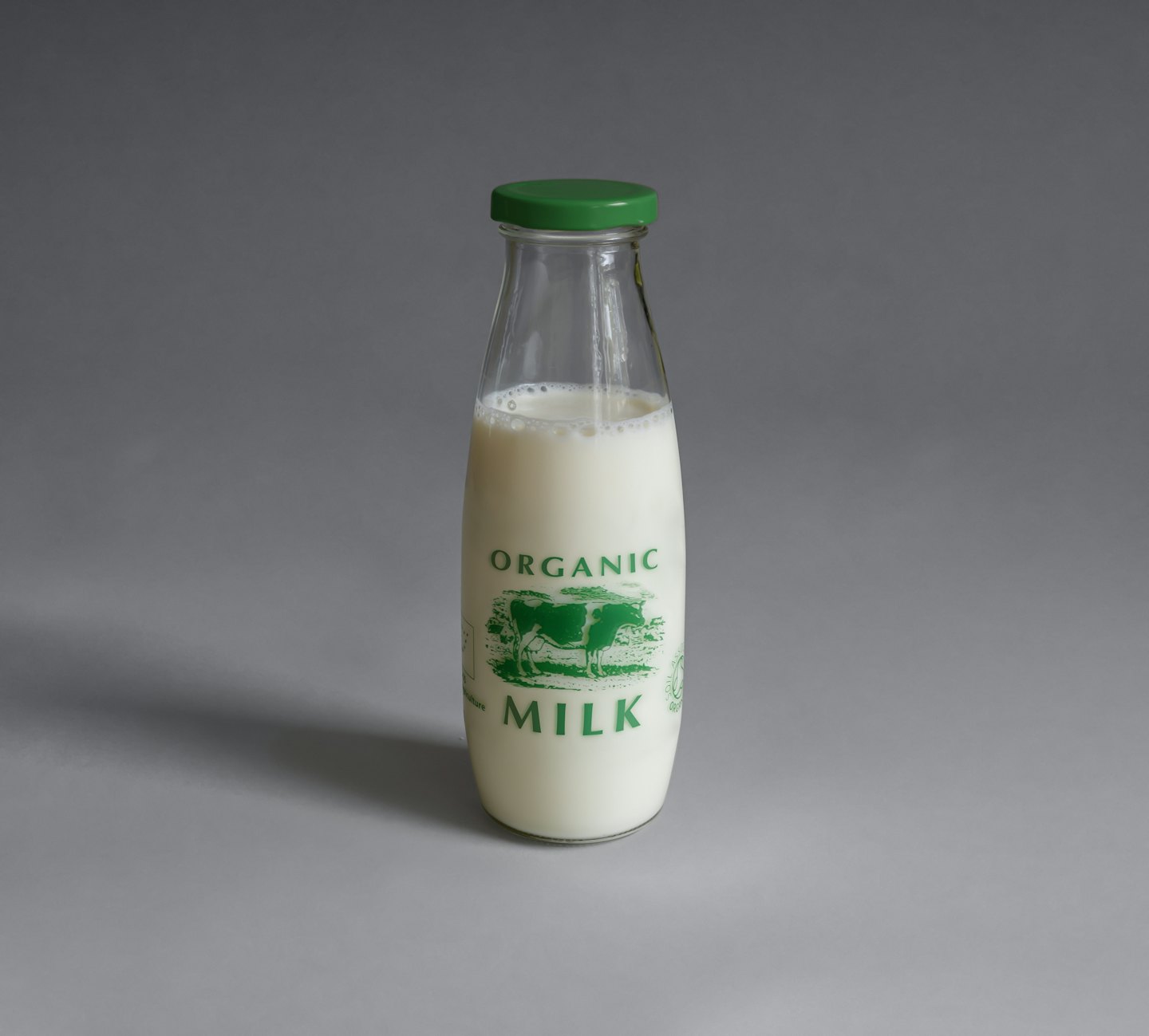 Bottiglia di vetro di latte biologico con tappo verde su superficie grigia.